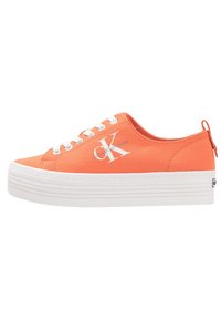 Orange canvas sneakers med vit plattformssula, med vita snören och en vit logotyp på sidan. Texturerad ovandel och dragflik vid hälen.