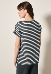 Camiseta de rayas grises con mangas cortas, corte relajado, amplia abertura en el cuello y puños enrollados. El material parece suave y liviano.