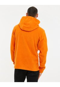 Sudadera de forro polar naranja con capucha, hombros caídos y puños acanalados. Textura suave, corte relajado y dobladillo inferior.