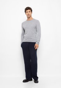 Grauer, gestrickter Pullover mit langen Ärmeln, kombiniert mit navyblauen weiten Hosen, verziert mit schwarzen Schuhen. Einfaches und vielseitiges Outfit-Design.