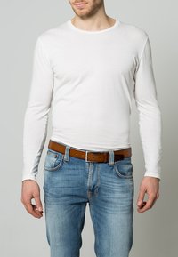 White long-sleeve shirt made of cotton, paired with light blue denim jeans and a brown leather belt. Simple design with a round neckline.