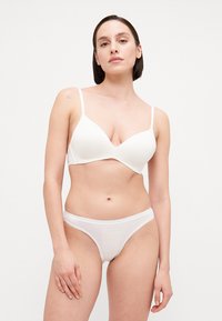 White seamless bra with a plunging neckline and adjustable straps, paired with matching white thong. Smooth fabric and minimalist design.
