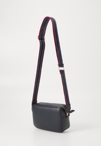 Morska plava kožna crossbody torba pravokutnog oblika, sa zlatnim patentnim zatvaračem i podesivim remenom koji ima crvene i crne pruge.