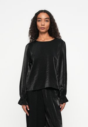 Haut noir, en satin, à manches longues avec une coupe décontractée, encolure ronde et poignets à volants, associé à un pantalon assorti.