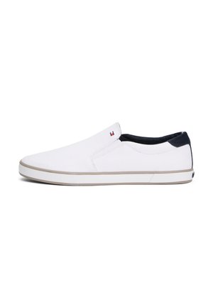 Białe buty slip-on z jasnobrązową podeszwą, czarnym kołnierzem na pięcie oraz małym logo w kolorach czerwonym, białym i niebieskim blisko otworu na białym tle.