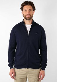 Pull zippé marine avec un col haut, des poignets côtelés et un petit logo sur la poitrine gauche. Matière douce et design ajusté.