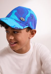 Mėlyna kepuraitė su marmuro raštu, įvairių mėlynos atspalvių, juodu logotipu priekyje ir išlenktu snapeliu.