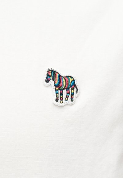 Μικρό κέντημα ζέβρας με πολύχρωμες ρίγες σε λευκό υφασμάτινο φόντο.