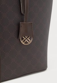 Καφέ τσάντα ώμου με σχέδιο και υφή, με δερμάτινο λουράκι και λεπτομέρειες χρυσού εμβλήματος.