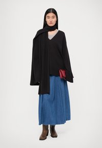 Pull noir oversized, jupe en denim bleu taille haute, bottines marron, et pochette rouge. Tissu lisse, design superposé, et manches larges.