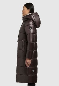 Long, dark brown puffer coat with a hood, featuring a quilted design, zippered pockets, and a logo patch on the sleeve. Smooth finish.