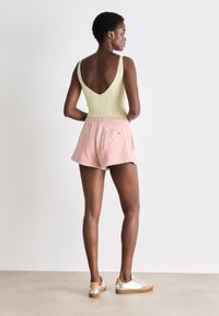 Bodysuit côtelé vert clair avec un dos en V profond, associé à un short rose clair à taille élastique avec une poche arrière et des baskets décontractées.