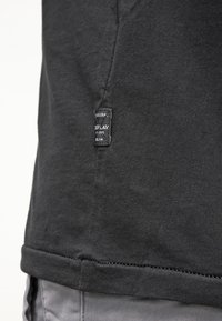 Black cotton t-shirt with a straight cut, featuring a sewn tag on the left side, and visible stitching along the hem and sleeve.