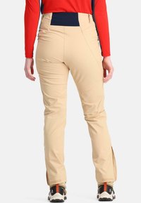 Beige buitenbroeken met een hoge tailleband en zijritsen, gecombineerd met zwarte en oranje wandelschoenen. Zachte textuur, slim fit.
