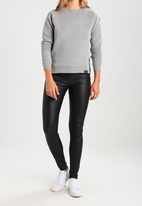 Pull gris côtelé avec un col rond et des manches longues, associé à des leggings noirs ajustés et des baskets blanches. Design simple et moderne.