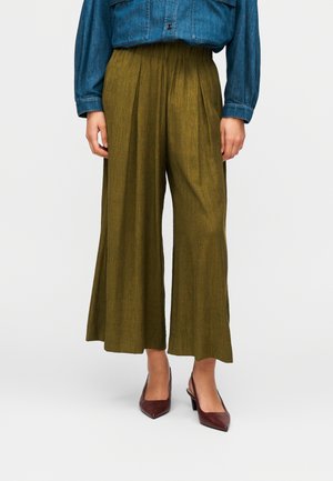 Pantalon large kaki en tissu texturé, avec plis à l'avant et ceinture élastique, associé à des talons pointus bordeaux.