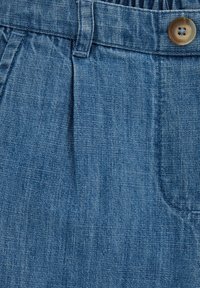 Heledates sinises toonis teksapüksid tekstuurse viimistlusega. Neil on volditud disain, nööpkinnitusega ja küljetaskud.