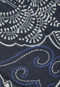 Donkere stof met ingewikkelde witte en blauwe cirkelpatronen, met spiralen en stippen, een gladde textuur en een effen diep marineblauwe achtergrond.