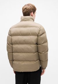 Puffjakke i khaki farve med en quiltet design, høj krave og elastiske manchetter, lavet af struktureret, let materiale.