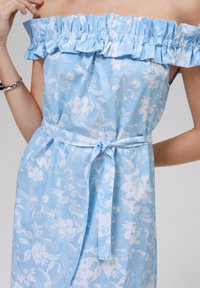 Abito blu floreale scollato sulle spalle con scollatura arricciata, fantasie bianche di fiori, vita cintrata con nodo e tessuto morbido.