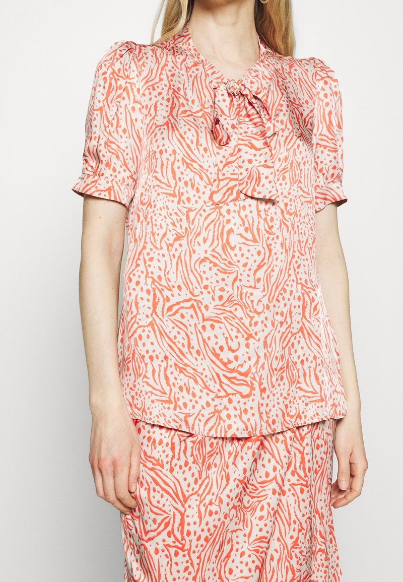 Krátký rukáv top z lehkého materiálu, s abstraktním vzorem v růžové a oranžové barvě, s detailem mašle na výstřihu a volným střihem.