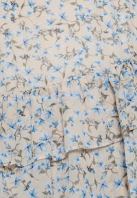 Tessuto floreale con fiori blu su uno sfondo beige, caratterizzato da un orlo arricciato. Il motivo consiste in delicati disegni floreali e foglie.