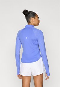 Αθλητική μπλούζα μακρυμάνικη σε ανοιχτό γαλάζιο με υφή στο μοτίβο των μανικιών, με όρθιο γιακά και μίνιμαλ λογότυπο στην πλάτη.