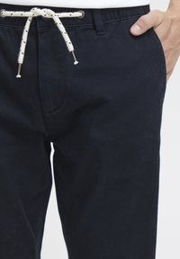Navy blue fabric pants featuring a drawstring closure with white and black accents, side pockets, and a slim-fit design.