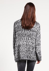 Svartvit mjuk tröja med lös passform, rund halsringning och långa ärmar; texturerat mönster ger visuell djup.