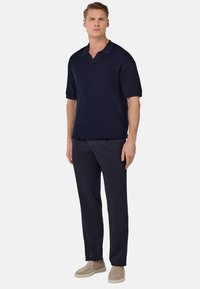 Navy ribbed short-sleeve polo shirt with a collar, paired with dark trousers and light beige slip-on shoes. Smooth texture, fitted design.