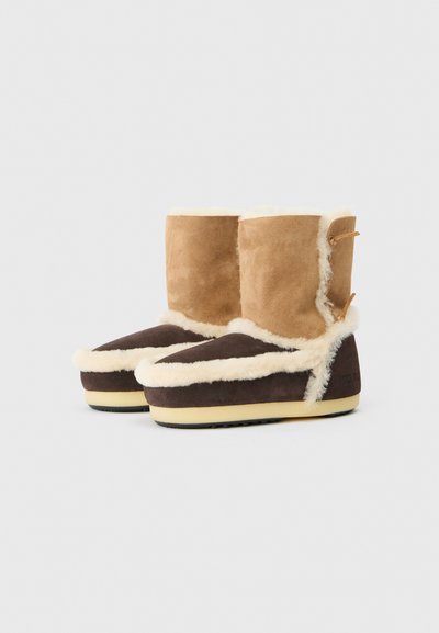 Botas de shearling marrones y tostadas con forro de piel de oveja, que cuentan con una parte superior de gamuza suave, una puntera de un marrón oscuro en contraste y suelas de goma claras.