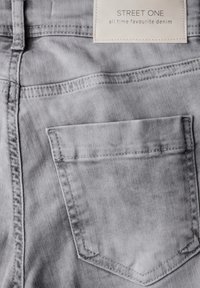 Jeans de mezclilla gris con un bolsillo trasero y una etiqueta que dice "STREET ONE, los vaqueros favoritos de todos los tiempos." Textura suave, diseño casual.