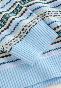 Lichtblauwe gebreide trui met geometrische patronen in groen, roze en zwart. Ribgebreide manchetten en zoom met een gladde textuur overal.