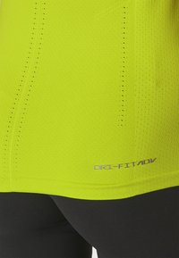 Camisa atlética amarilla brillante con un acabado texturizado, que presenta orificios de ventilación a lo largo del costado y la marca "DRI-FIT" en el dobladillo.