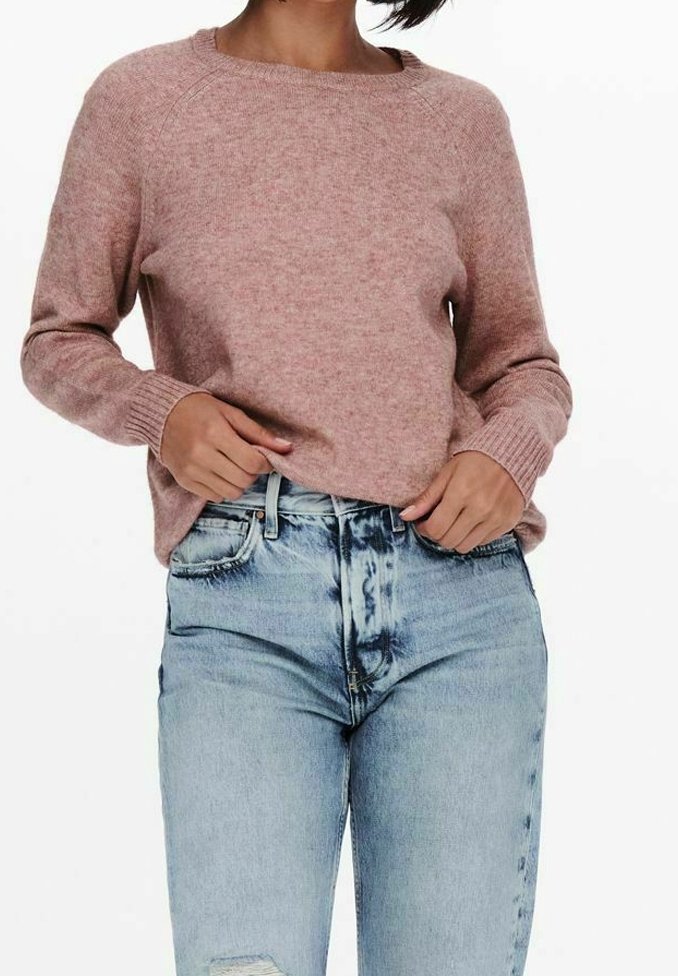 Pull en maille rose à manches longues, col rond et poignets côtelés, associé à un jean bleu clair déchiré à taille haute.