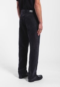 Vaqueros de denim negros con un ajuste recto, diseño de cinco bolsillos y parche de la marca en la parte trasera de la cintura. Textura suave y estilo clásico.