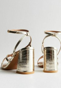 Metalen gouden sandalen met hakken, een krokodillenstructuur en gekruiste enkelbanden. Blokhak ontwerp, zachte binnenvoering en open teen stijl.
