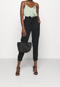 Ljusgrön satinkami, svarta högmidjade byxor med knytbälte och svart handväska. Svarta klacksandaler fulländar outfiten.