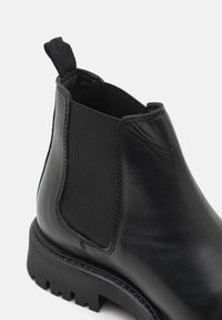 Stivale ankle in pelle nera con pannelli laterali elasticizzati, linguetta, superficie testurizzata e una suola in gomma spessa e scanalata.