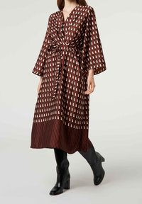 Robe portefeuille à motif géométrique marron et beige, dotée d'une ceinture nouée à la taille, d'un col en V et de manches larges. Associée à des bottes à talons noires.