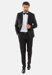 Tuxedo nero con rever in raso, camicia bianca e papillon nero. Pantaloni aderenti e scarpe eleganti nere lucidate. Design su misura.