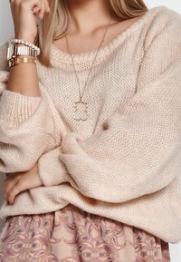 Ljusrosa stickad tröja med vida ärmar, lager ovanpå en mönstrad kjol. Outfiten har guldsmycken som accent, inklusive ett delikat halsband.