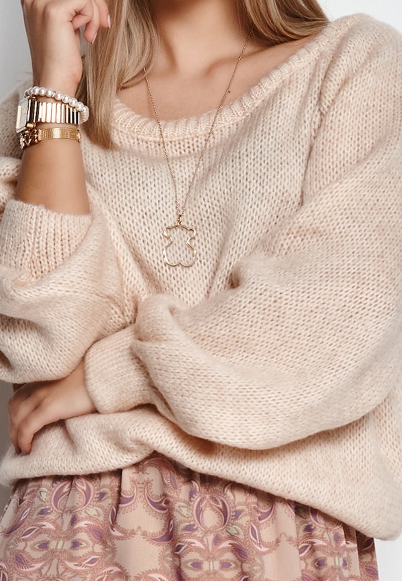 Ljusrosa stickad tröja med vida ärmar, lager ovanpå en mönstrad kjol. Outfiten har guldsmycken som accent, inklusive ett delikat halsband.
