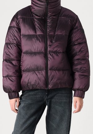 Persona con chaqueta acolchada de color púrpura oscuro y brillante, con puños elásticos y cremallera negra, combinada con jeans gris oscuro.