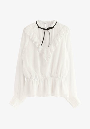 Blouse blanche à manches longues avec détail en dentelle froncée en forme de V, taille cintrée, poignets smockés et fine ceinture noire à nouer au niveau du col.