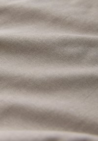 Prim-plan al unei țesături bej deschis cu o textură fină de tricot vizibilă și pliuri moi care creează umbre delicate.