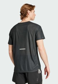 Camiseta deportiva negra con patrón texturizado, mangas cortas, acentos reflectantes y un ajuste relajado. Adecuada para ropa deportiva.