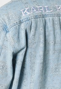 Light blue denim jacket with paisley pattern, embroidered "KARL" at the back collar, and textured details on the fabric.
