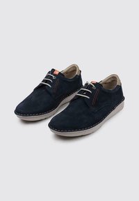Zapatos de ante azul marino con punta redondeada, costuras ligeras y un diseño con cordones. Incluyen un forro interior beige y un sutil acento naranja.