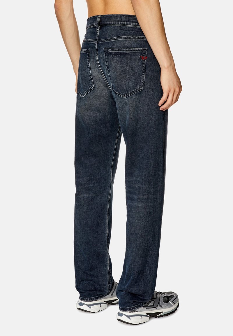 Dunkelblaue Jeans aus Denim mit lockerer Passform, ausgestattet mit fünf Taschen, dezentem Verblassen und einem Bund mit Gürtelschlaufen. Getragen mit Turnschuhen.